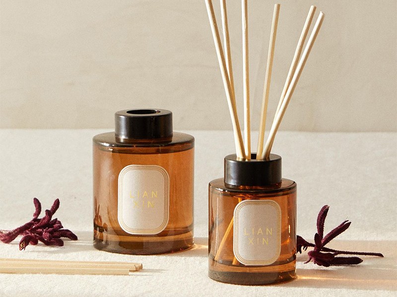 custom reed diffuser bottles in amber glass, one sealed with a black cap and one filled with reeds