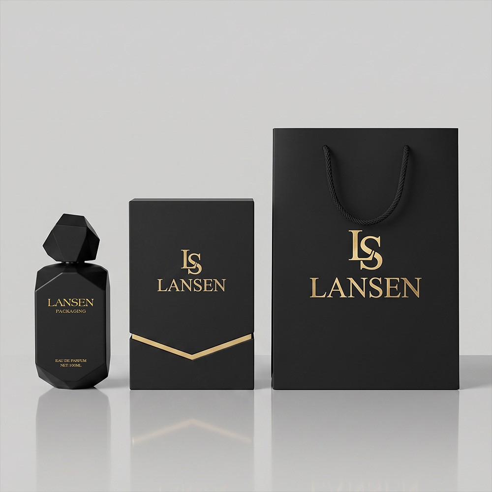 100ml black irregular perfume bottle beside a matte black rigid gift box with a gold chevron band and a matching black paper bag