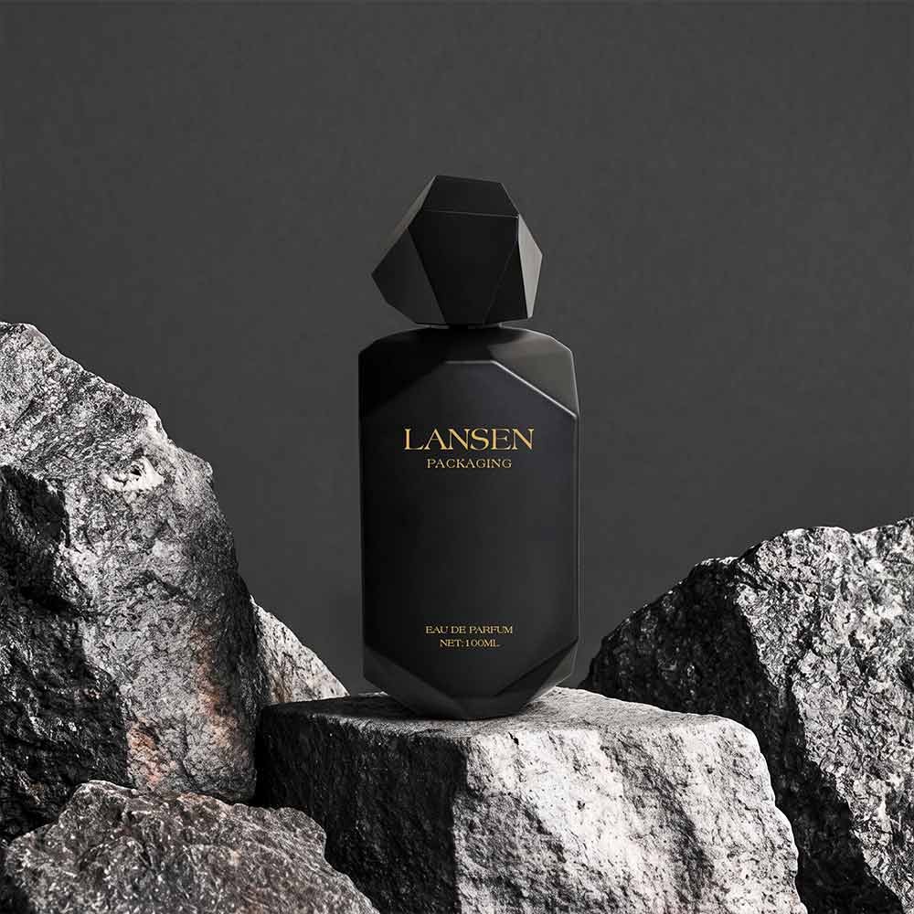 100ml matte black faceted perfume bottle with a polyhedron cap displayed on rough rock against a grey backdrop