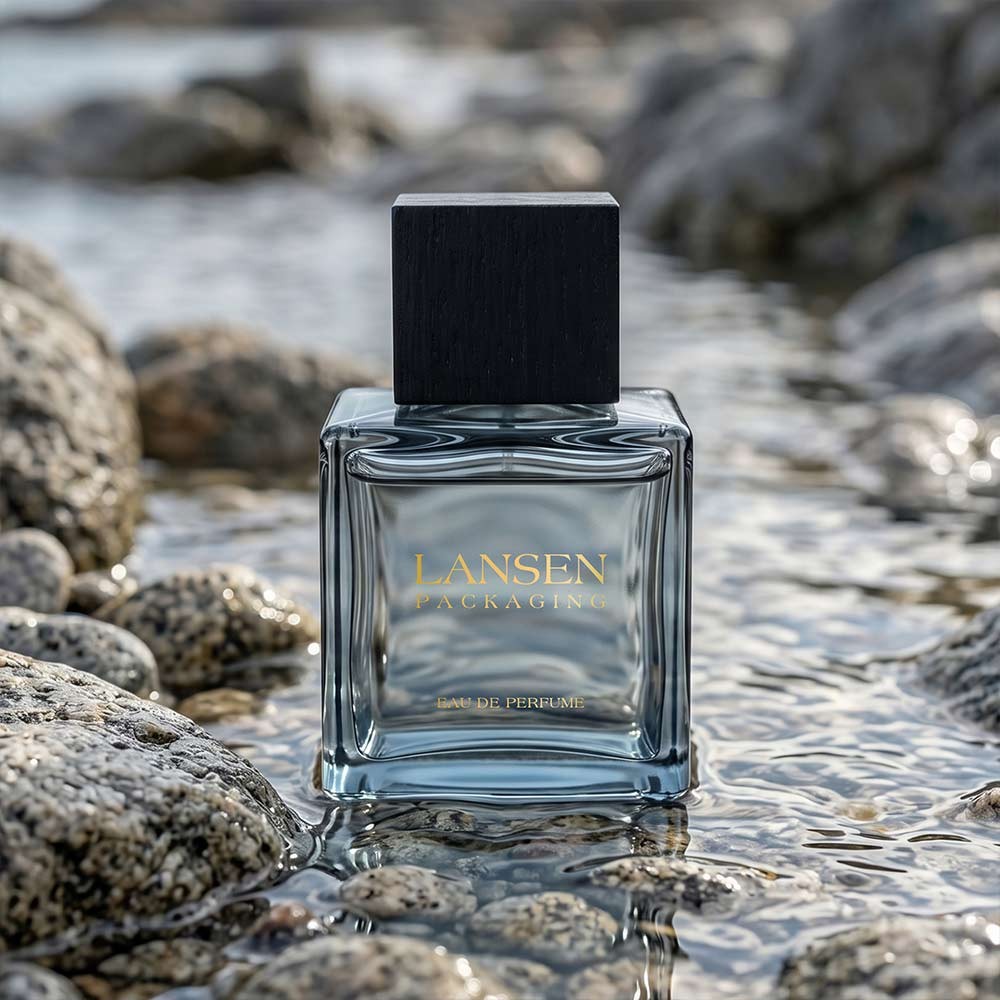 100ml square glass perfume bottle with gold lettering applied directly to the glass and a black wooden square cap, standing in shallow water