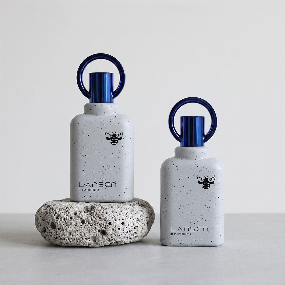 two 50ml speckled ivory perfume bottles with blue ring caps displayed on a porous stone